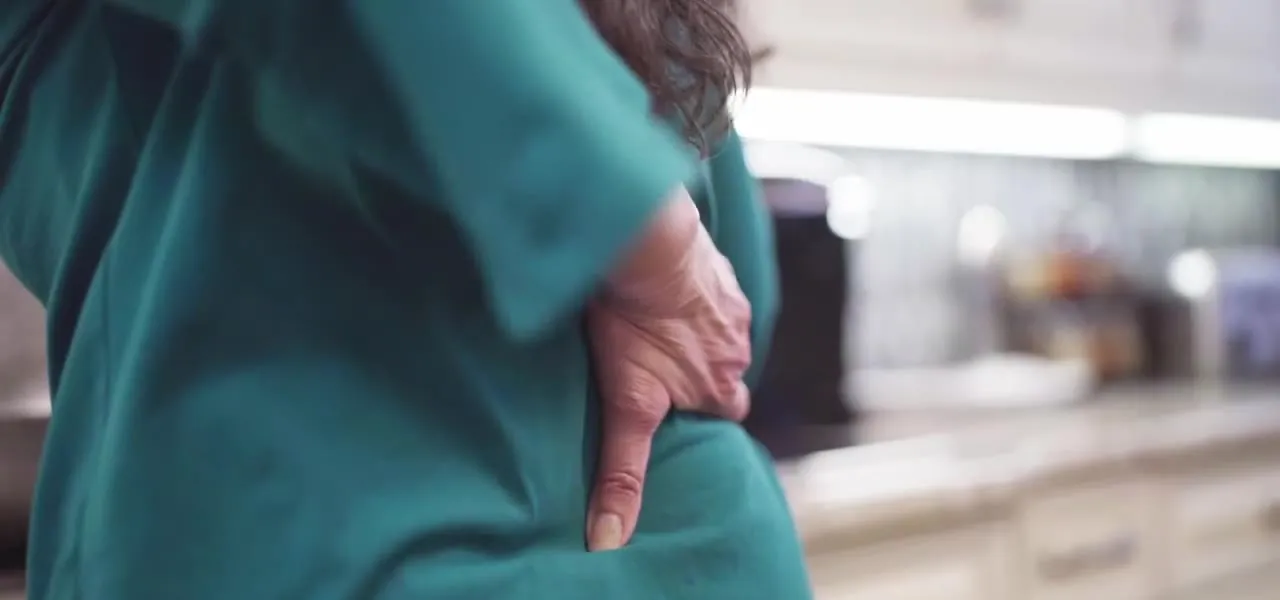 A woman pressing a hand to her lower back in her kitchen