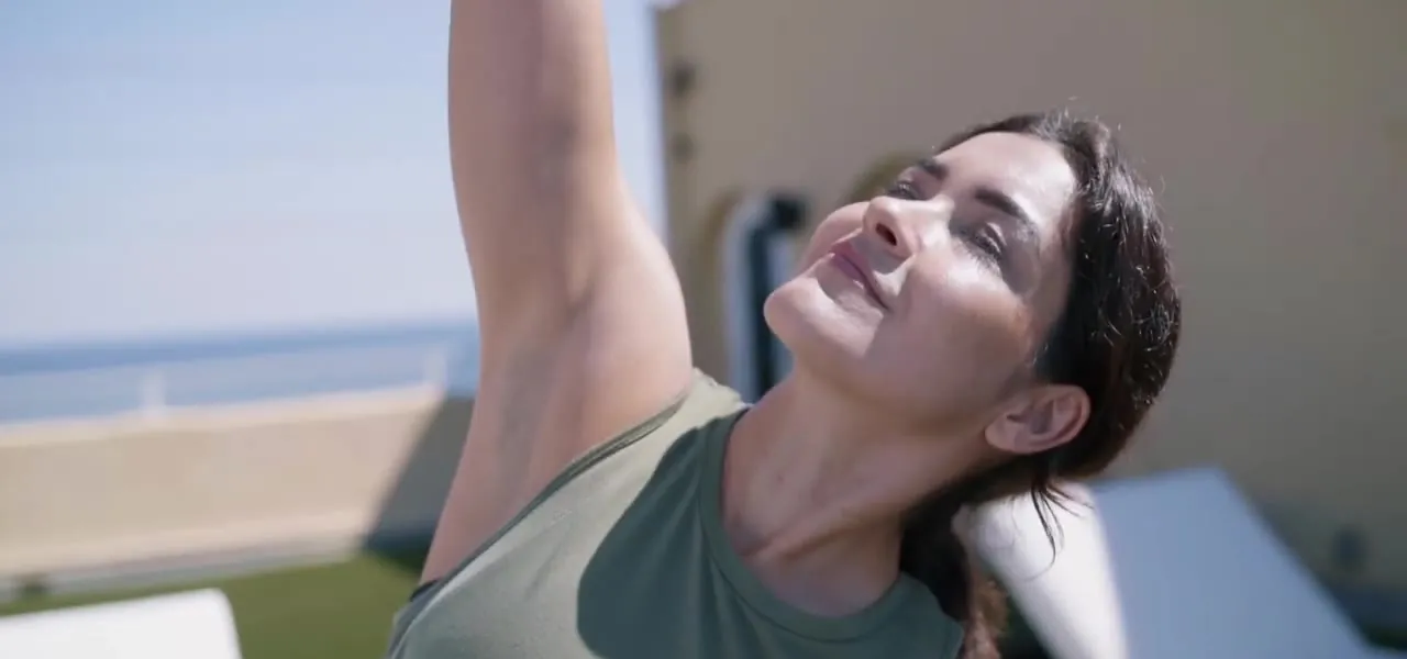 A woman stretching outdoors in the sun, arms overhead